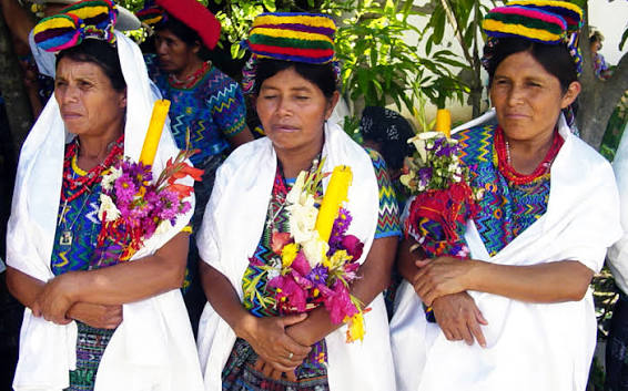 Women in traditional woven clothing holding flowers at a ceremony