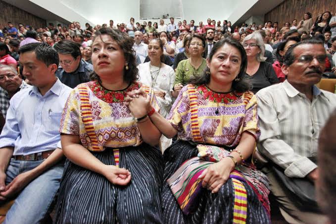 Women in traditional embroidered blouses seated among a large audience